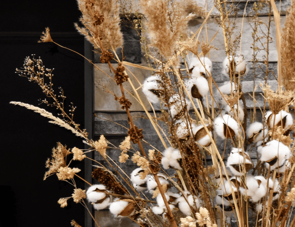 A close-up of dried flowers and cotton branches arranged together, set against a textured stone background.